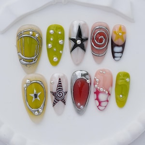 May include: A set of ten press-on nails featuring diverse designs including lime green, red, and white bases with silver metallic accents, star motifs, spiral patterns, and small silver beads. The collection displays various shapes and artistic details.