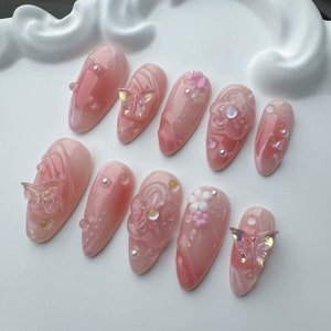 Op de afbeelding: Set van tien roze en witte kunstnagels met verschillende bloemen- en vlindermotieven.