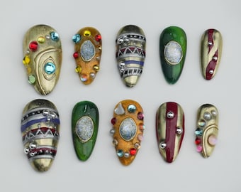 Könnte beinhalten: Eine Sammlung von zehn verzierten, mandelförmigen Nageldesigns. Jeder Nagel hat eine einzigartige Kombination von Farben, darunter Gold, Grün und Rot, mit Verzierungen wie Strasssteinen und metallischen Akzenten. Die Designs variieren in Muster und Stil.