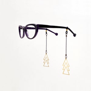 May include: Purple cat-eye glasses with black chain and gold triangle charms hanging from the arms.