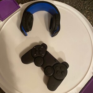 Op de afbeelding: Een zwarte en blauwe gaming-headset en een zwarte videogamecontroller op een wit oppervlak.