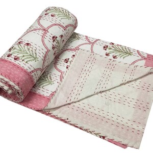 May include: A white and pink kantha quilt with a floral pattern. The quilt is hand-stitched and has a traditional Indian design.