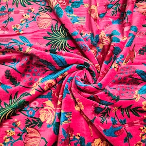 May include: Pink fabric with a floral print featuring birds, leaves, and flowers. The fabric is folded and twisted, showing the texture of the material.