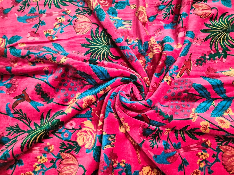 May include: Pink fabric with a floral print featuring birds, leaves, and flowers. The fabric is folded and twisted, showing the texture of the material.