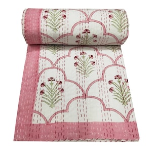 May include: A pink and white kantha quilt with a floral pattern. The quilt is made of cotton and is hand-stitched. It is a traditional Indian textile.