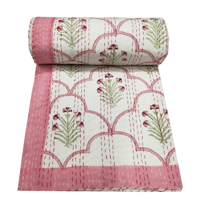 May include: A pink and white kantha quilt with a floral pattern. The quilt is made of cotton and is hand-stitched. It is a traditional Indian textile.