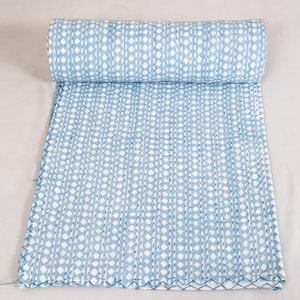 May include: A rolled-up, light blue and white patterned quilt. The quilt features a repeating pattern of vertical lines and diamond shapes. The edges are finished with a decorative stitch.