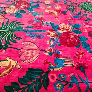 May include: A pink fabric with a floral pattern featuring pink, red, yellow, and green flowers, birds, and a deer. The fabric has a velvet-like texture.