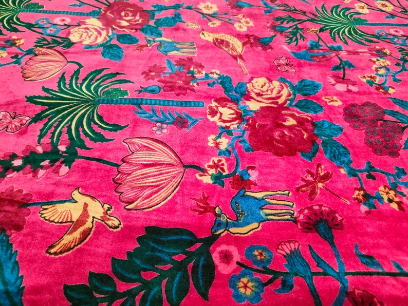 May include: A pink fabric with a floral pattern featuring pink, red, yellow, and green flowers, birds, and a deer. The fabric has a velvet-like texture.