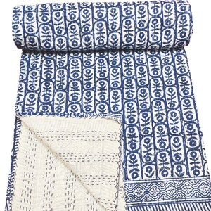 K&ouml;nnte beinhalten: Eine blaue und wei&szlig;e Kantha-Steppdecke mit einem Blumenmuster. Die Decke ist in der H&auml;lfte gefaltet und der Stoff ist weich und strukturiert.