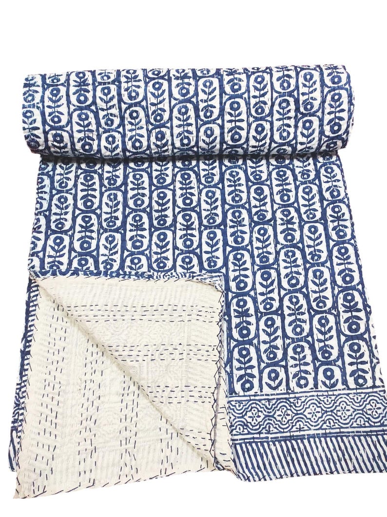 K&ouml;nnte beinhalten: Eine blaue und wei&szlig;e Kantha-Steppdecke mit einem Blumenmuster. Die Decke ist in der H&auml;lfte gefaltet und der Stoff ist weich und strukturiert.