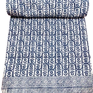 K&ouml;nnte beinhalten: Eine wei&szlig;e und blaue Kantha-Steppdecke mit einem floralen Muster. Die Steppdecke ist in der H&auml;lfte gefaltet und hat einen dekorativen Rand.