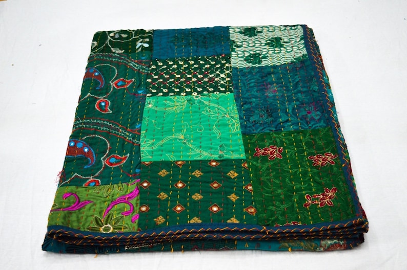 May include: A patchwork quilt featuring a mix of green and blue fabrics. The quilt is made up of squares of varying sizes and patterns, and is embellished with embroidery and sequins.