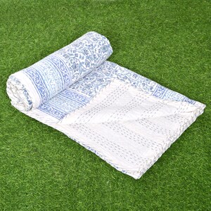 May include: A white and blue kantha quilt with a floral pattern. The quilt is folded and rolled up, and the fabric is soft and textured.