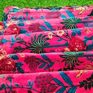 May include: Pink fabric with a floral print featuring blue and green leaves, pink flowers, and palm trees. The fabric is folded in layers.