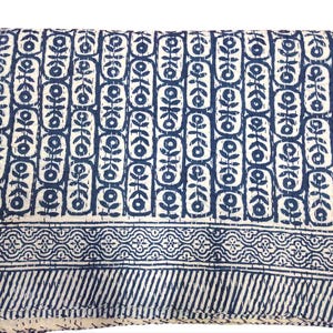 K&ouml;nnte beinhalten: Eine wei&szlig;e Baumwolldecke mit einem blauen und wei&szlig;en geometrischen Muster. Die Decke hat einen Rand mit einem sich wiederholenden Muster aus Blumen und Bl&auml;ttern.