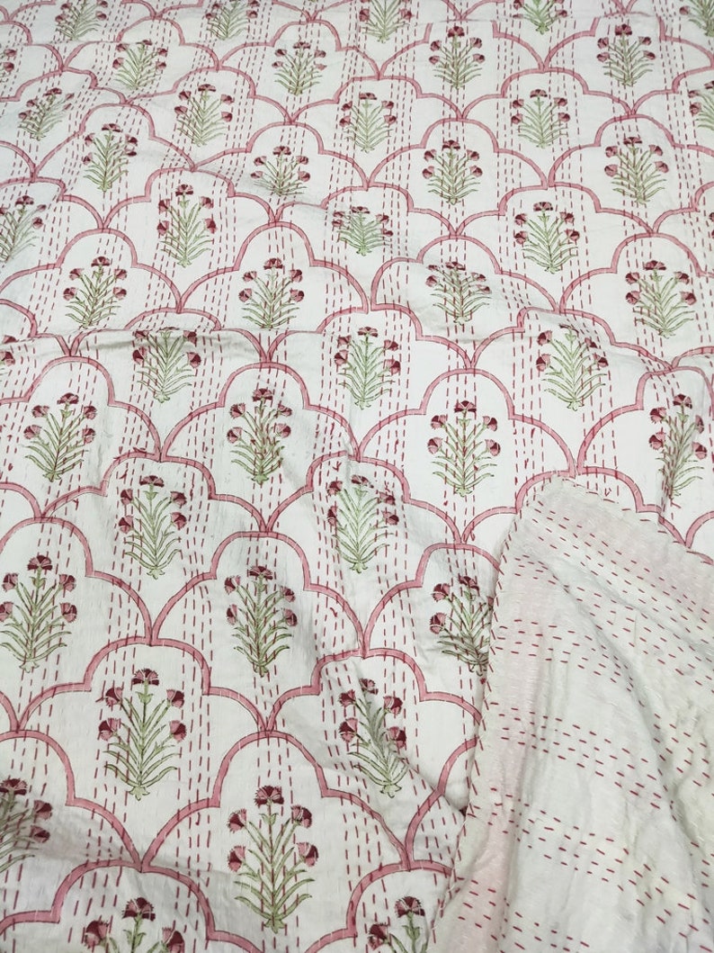 May include: White cotton fabric with a pink and green floral pattern. The fabric is quilted with a pink thread and has a scalloped design.