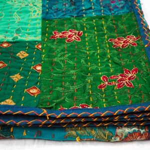 May include: A green and blue patchwork quilt with embroidered floral designs. The quilt is folded in thirds and has a blue and orange trim.