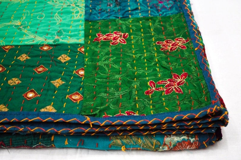 May include: A green and blue patchwork quilt with embroidered floral designs. The quilt is folded in thirds and has a blue and orange trim.