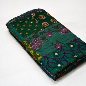 May include: A green and purple kantha quilt with floral embroidery and mirror embellishments. The quilt is folded in half and is made of patchwork fabric.
