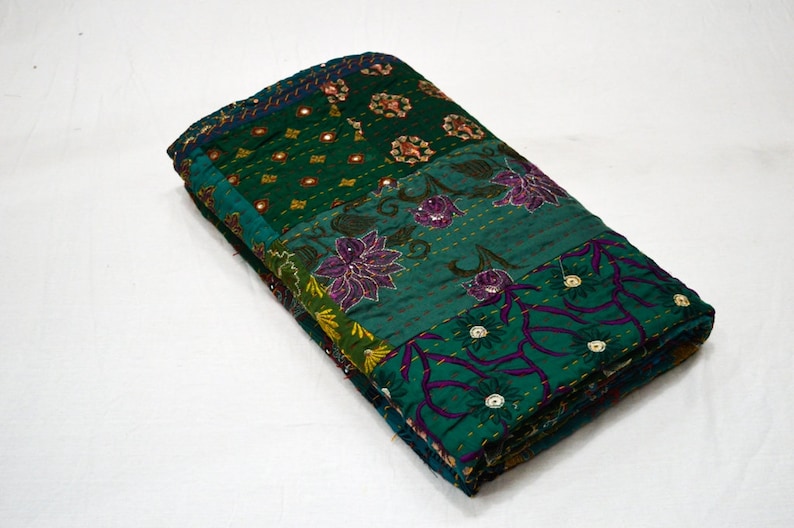 May include: A green and purple kantha quilt with floral embroidery and mirror embellishments. The quilt is folded in half and is made of patchwork fabric.