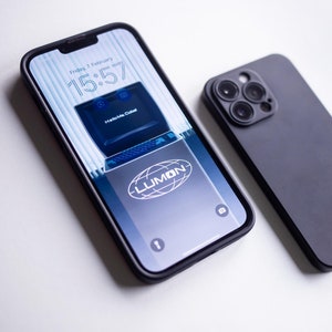 Può includere: Due custodie per iPhone nere, una con il retro trasparente e un'immagine di schermo di computer retrò con il testo "Hello Me Dubai" e "LUMON" sullo schermo, e l'altra con il retro nero solido e un rigonfiamento della fotocamera con tre obiettivi.