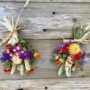 May include: Two small bouquets of dried flowers tied with twine. The bouquets are made up of purple, pink, yellow, orange, and red flowers. The bouquets are on a wooden background.