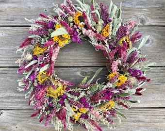 May include: A dried flower wreath with purple, pink, and yellow flowers. The wreath is made with dried sunflowers, lavender, and other wildflowers.