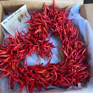 K&ouml;nnte beinhalten: Eine Schachtel gef&uuml;llt mit getrockneten roten Chilischoten. Die Chilischoten sind in Form eines Kranzes angeordnet. Eine kleine Karte mit dem Text "The Garlic People" ist in der Schachtel sichtbar.
