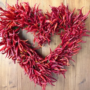 K&ouml;nnte beinhalten: Ein herzf&ouml;rmiger Kranz aus getrockneten roten Chilischoten.