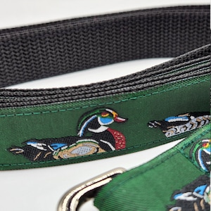 May include: A green dog leash with a black webbing and a silver clip. The leash has a repeating pattern of colorful wood ducks.