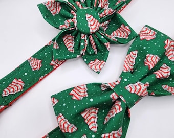 May include: A green dog collar and accessories set with a Christmas tree pattern. The set includes a collar, a flower-shaped accessory, and a bow tie. The collar is green with a red interior and a black buckle.