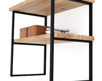 May include: A two-tier shelving unit featuring a black metal frame and two light-colored wooden shelves with a natural grain. The bottom shelf holds two brown woven baskets and a stack of folded grey and white fabric items.