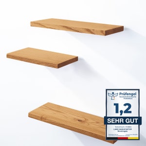 Peut inclure: Trois étagères en bois montées sur un mur blanc. Les étagères sont en bois naturel avec une finition brun clair. Les étagères sont de tailles différentes, la plus haute étant la plus grande et la plus basse étant la plus petite. Les étagères sont vides.