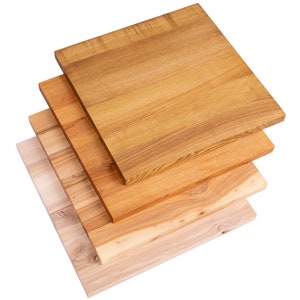 May include: A stack of five square wooden planks in varying shades of brown and tan. The planks are arranged diagonally, showcasing the natural wood grain and color variations. The top plank is a medium brown, while the bottom is a light tan.