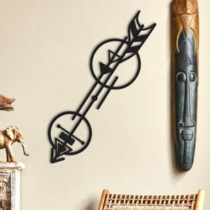 Puede incluir: Arte de pared de metal negro con una flecha estilizada con formas geométricas y círculos. La flecha está montada en una pared beige con una silla de madera y una figurita de elefante decorativa en primer plano.