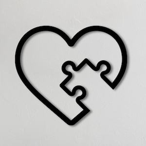 May include: Black metal wall decor in the shape of a heart with a puzzle piece inside. The heart is on a white wall above a gray couch with green throw pillows.