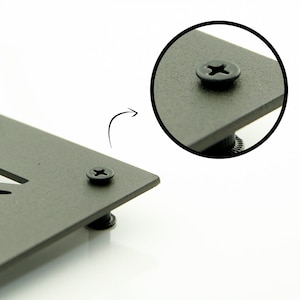 Op de afbeelding: Een close-up van een zwarte metalen plaat met een schroef in het midden. De schroef heeft een kruiskop en is omgeven door een zwarte kunststof ring.