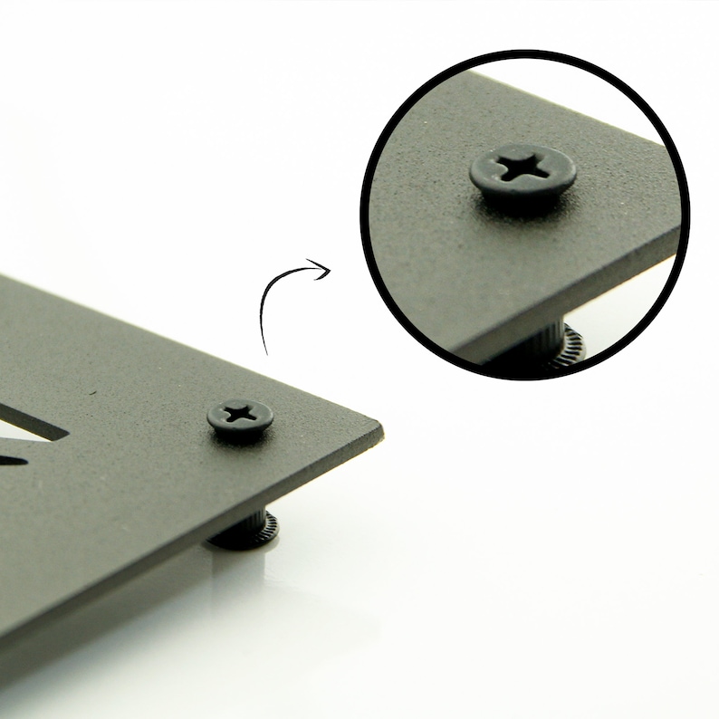 Op de afbeelding: Een close-up van een zwarte metalen plaat met een schroef in het midden. De schroef heeft een kruiskop en is omgeven door een zwarte kunststof ring.