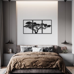 Op de afbeelding: Zwarte metalen wandkunst met een silhouet van een boom met takken die zich over drie panelen uitstrekken. De kunst wordt getoond boven een bed met bruine beddengoed in een moderne slaapkamer.