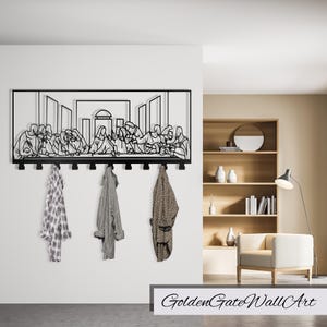 Puede incluir: Arte de pared de metal negro que representa La &Uacute;ltima Cena con un perchero debajo. El arte est&aacute; montado en una pared blanca con una estanter&iacute;a de madera y una silla en el fondo.
