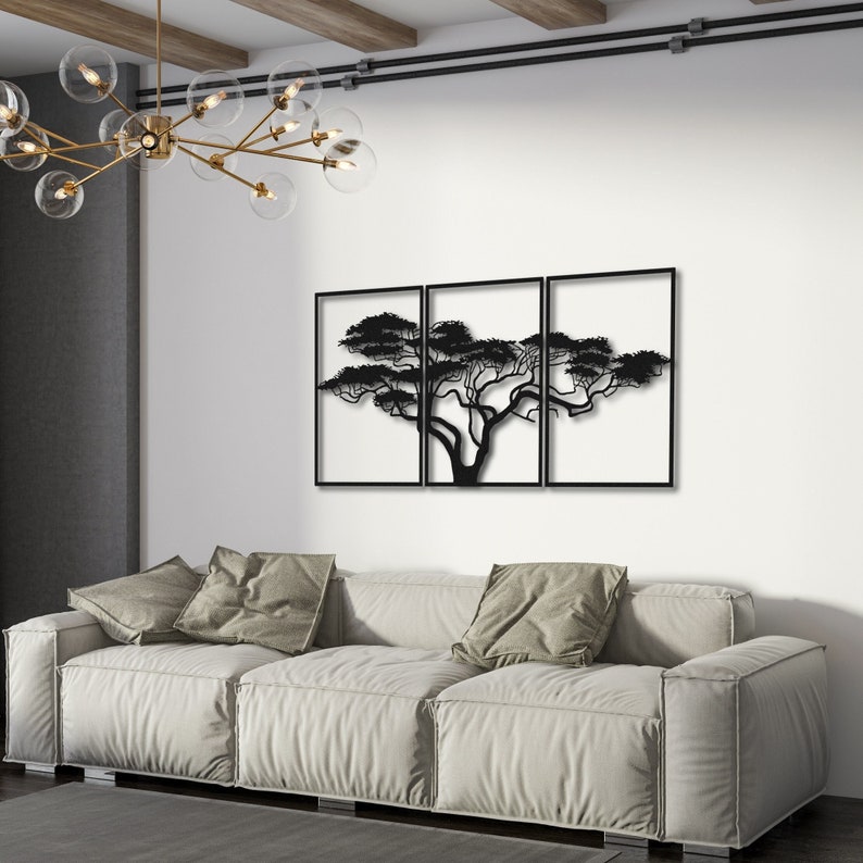Op de afbeelding: Een driedelig metalen wandkunstwerk met een zwart silhouet van een boom met uitgestrekte takken. De kunst is gemonteerd op een witte muur boven een lichte bank.