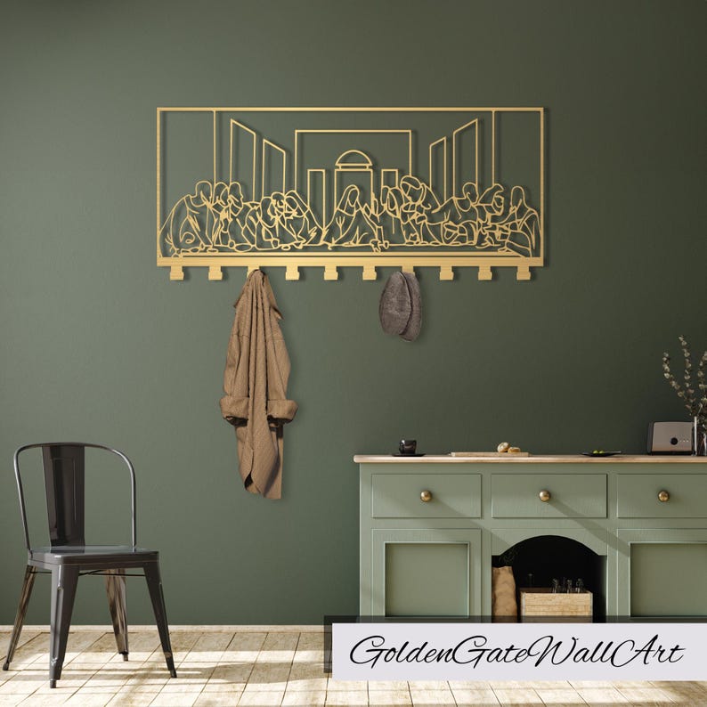 Puede incluir: Arte de pared de metal dorado que representa la &Uacute;ltima Cena con ganchos para colgar abrigos y sombreros. El arte est&aacute; montado en una pared verde con una silla y un gabinete en el fondo.