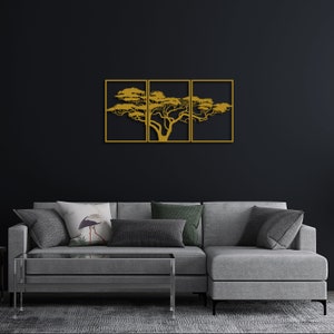 Op de afbeelding: Een gouden metalen wandsculptuur van een boom met takken die zich uitstrekken in drie afzonderlijke frames. De sculptuur hangt aan een zwarte muur boven een grijze hoekbank.