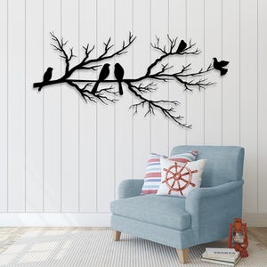 May include: A black metal wall art piece depicting a tree branch with several birds perched on it. The birds are in silhouette against a white wall. The artwork is a decorative element for a home.