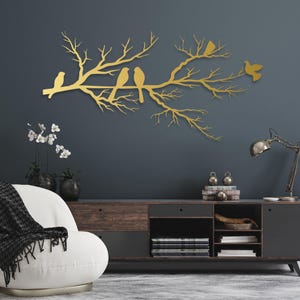 May include: A gold-colored metal wall art piece depicting a tree branch with several birds perched on it. The birds and branches are in a silhouette style, creating a decorative and artistic element for home decor.