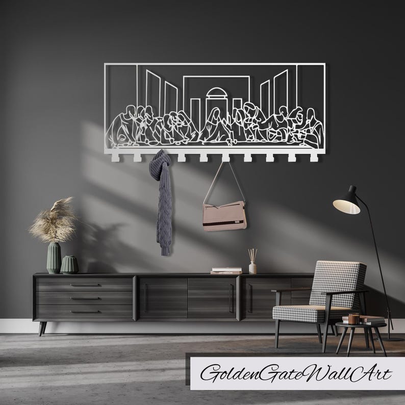 Puede incluir: Arte de pared de metal blanco que representa La &Uacute;ltima Cena con un perchero debajo. El arte est&aacute; montado en una pared gris con una c&oacute;moda de madera y una silla en primer plano.