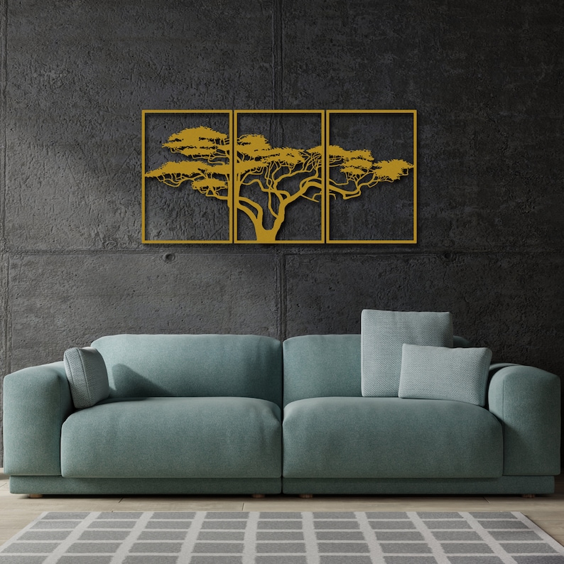 Op de afbeelding: Een driedelig metalen wandkunstbeeld met een gestileerde boom met gouden takken en bladeren tegen een donkergrijze muur. Het beeld is gemonteerd boven een teal-kleurige bank met twee kussens.