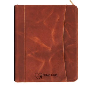 May include: A brown leather portfolio with a zipper closure. The portfolio has a heart and EKG design with the name "Robert Smith" engraved on the front. The leather has a textured appearance.