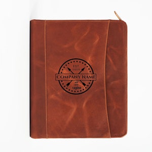 May include: Brown leather portfolio with a zipper closure. The front features a black logo with the text "EST. 2009 COMPANY NAME add your tagline".